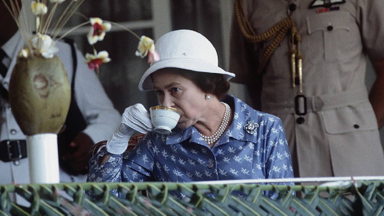 la reina Isabel tomando té en Nauru, Micronesia sola con vestido azul con puntos blancos